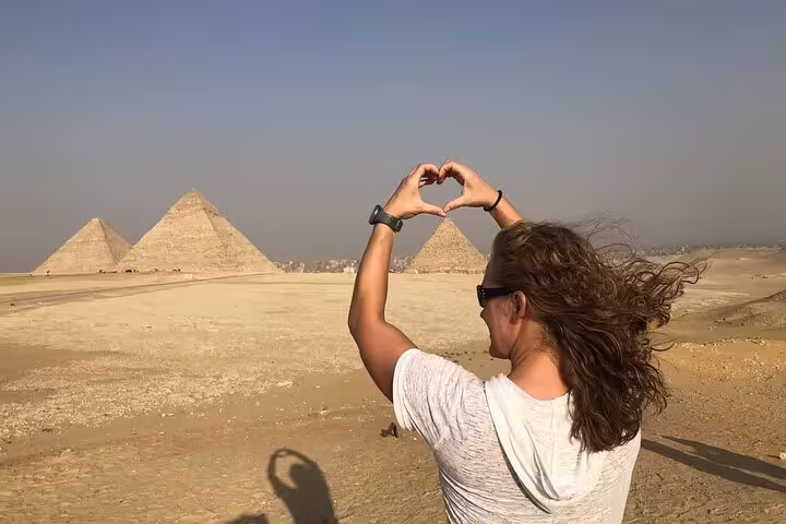 Tourist making heart hands toward Giza pyramids during a Cairo Airport layover tour with private transfer and guide