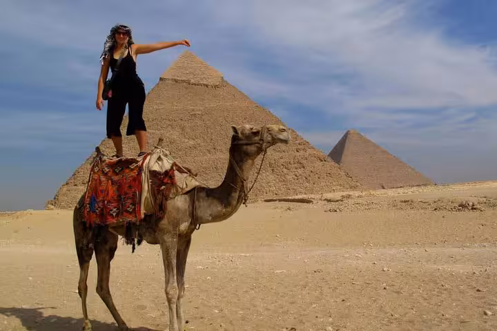 Tourist standing on a camel with Giza Pyramids backdrop on private Cairo day trip from Hurghada, Makadi Bay, Soma Bay
