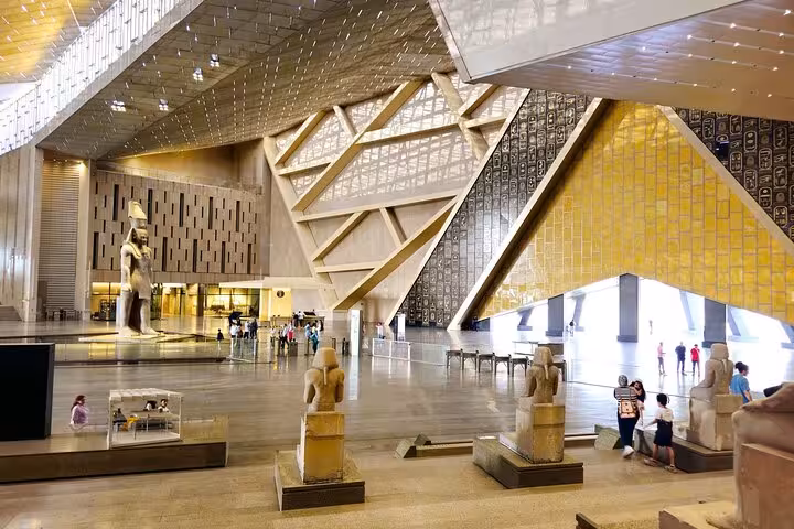 Wide view of Grand Egyptian Museum interior with statues and golden facade, Cairo day trip by plane from Marsa Alam