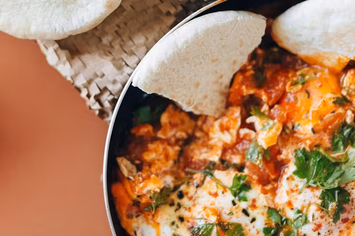 Explore Cairo's rich flavors with a spicy shakshuka dish, accompanied by fresh pita bread on the food tour.