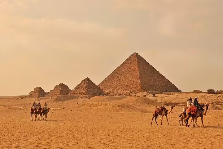 Camel caravan crossing the Giza desert with the pyramids in Cairo, ideal for a 2-day Cairo short break