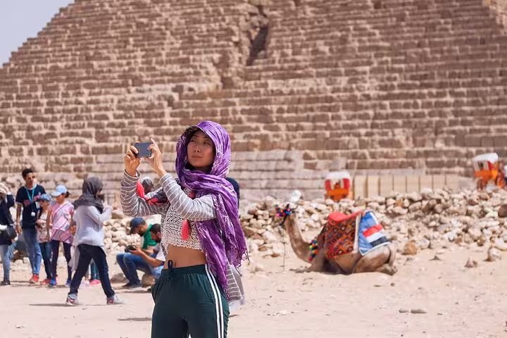 Traveler taking photos near the Giza Pyramid complex with camels on a Cairo day tour from Sharm by bus