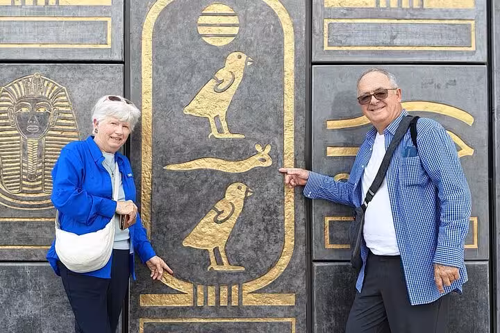 Travelers posing by pharaonic gold hieroglyph wall at Giza, VIP Pyramids and Grand Egyptian Museum tour