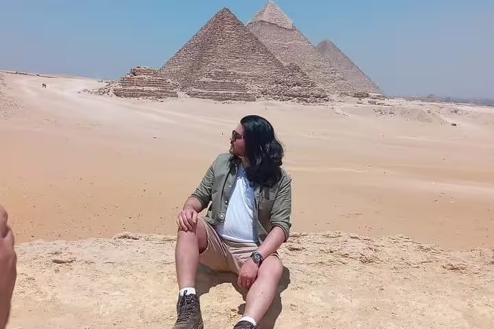 Traveler seated in Sahara sand with Giza Pyramids behind, Cairo from Luxor VIP first class train tour