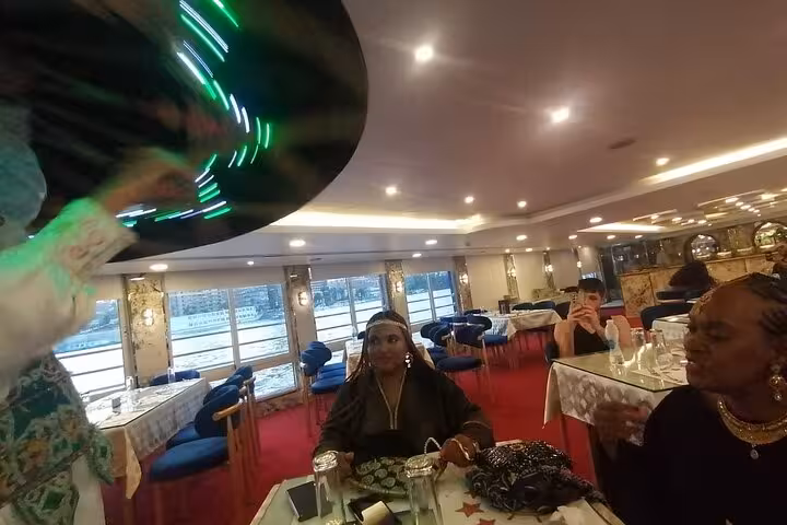 Guests enjoying Cairo Nile dinner cruise entertainment as a tanoura dancer spins during onboard folklore show