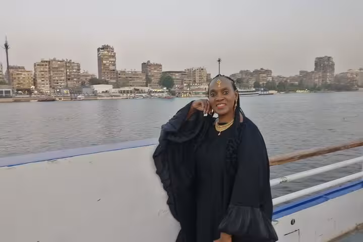 Traveler posing on Cairo Nile dinner cruise with city skyline backdrop, evening sailing and folklore show experience