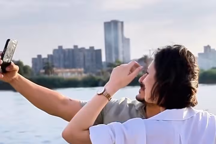 Couple taking a selfie on a Cairo Nile dinner cruise with the city skyline in the background during golden hour