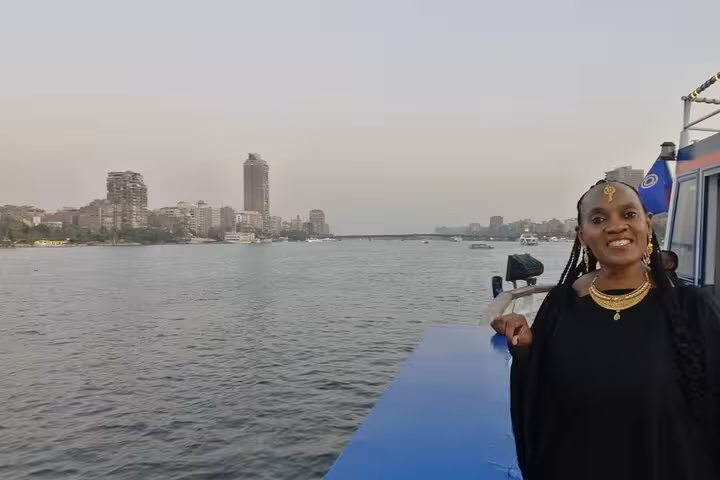 Guest on Cairo Nile dinner cruise deck at sunset with river skyline, belly dancing and folklore show onboard