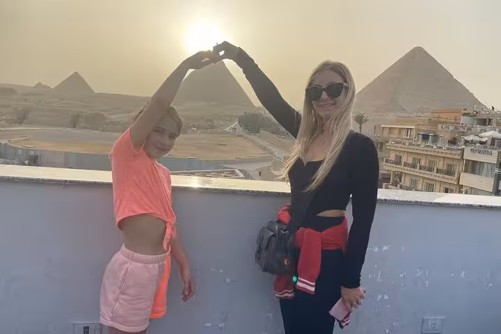 Guests pose on a rooftop with Pyramids of Giza at sunset on a Cairo private tour with Egyptian lunch