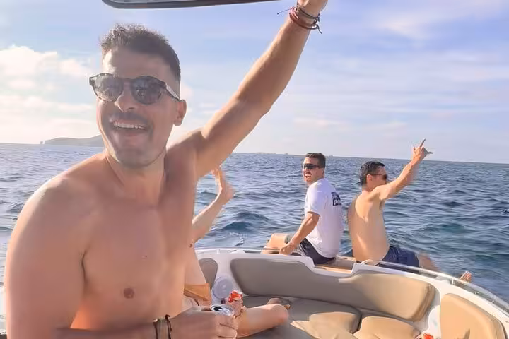 Group of friends enjoying a sunny boat tour on the turquoise waters of Cala Bassa and Cala Comte, Ibiza.