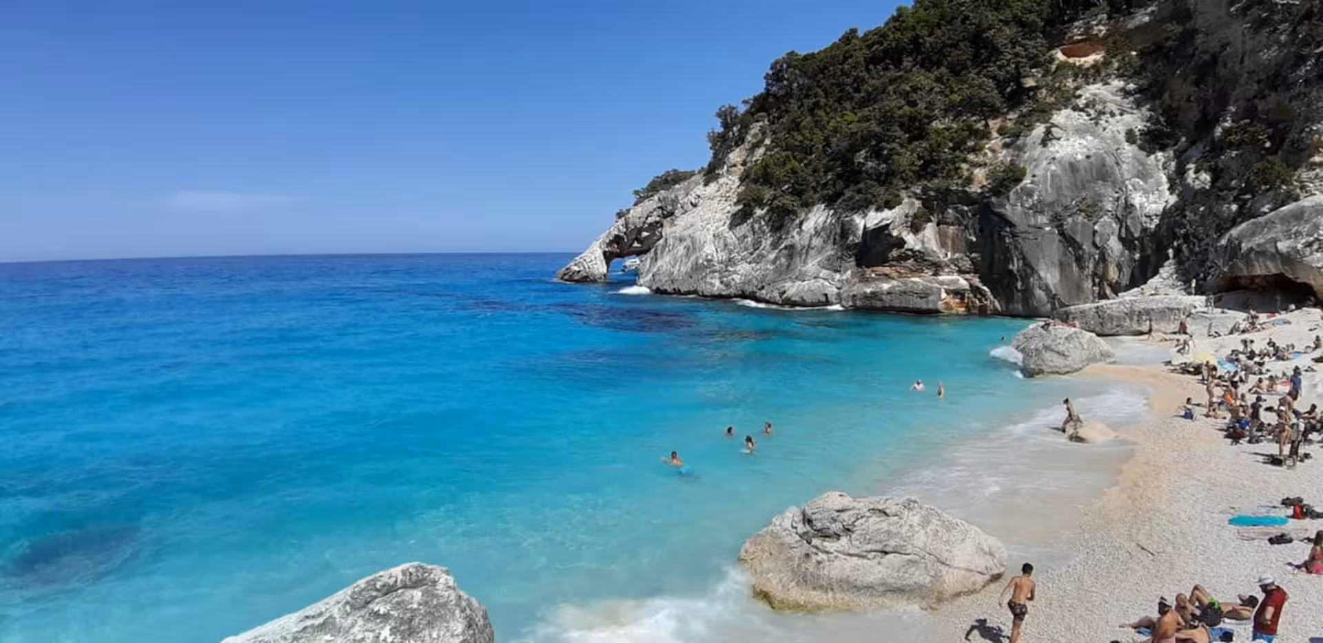 Tourists enjoying the pristine beach at Cala Goloritzè, surrounded by azure sea and dramatic rocky cliffs.