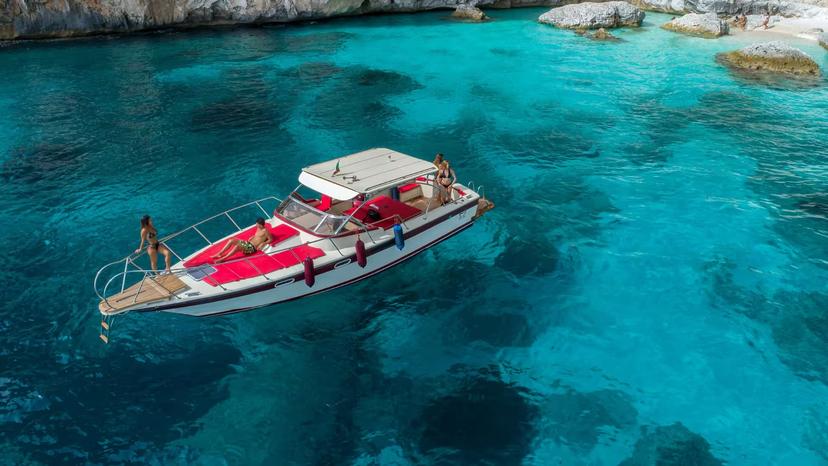 Tourists enjoying a boat excursion on crystal-clear waters near Cala Gonone in the Gulf of Orosei, Sardinia.