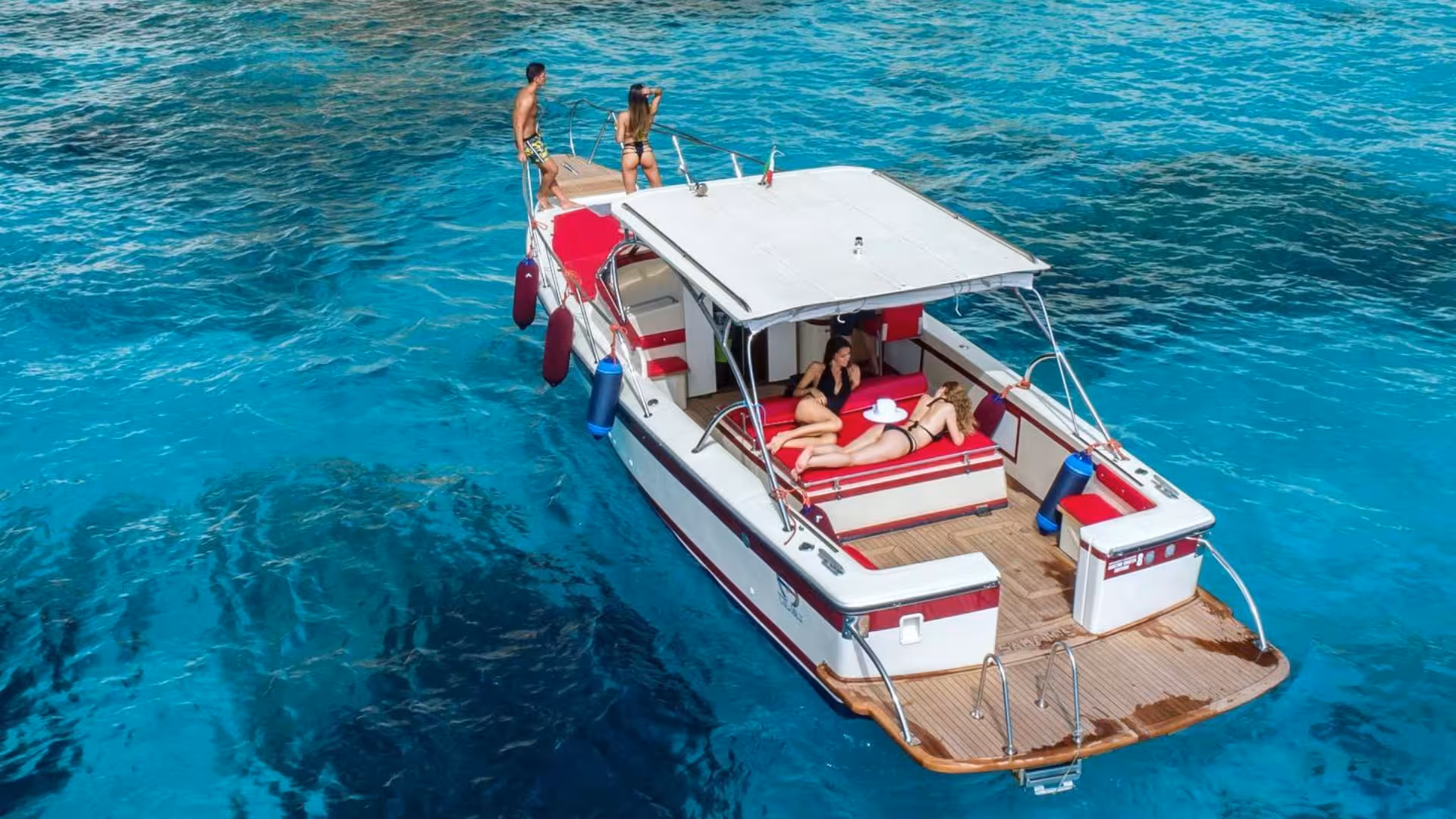 Luxurious boat with sunbathers cruising the crystal-clear waters of Gulf of Orosei on a Cala Gonone tour.