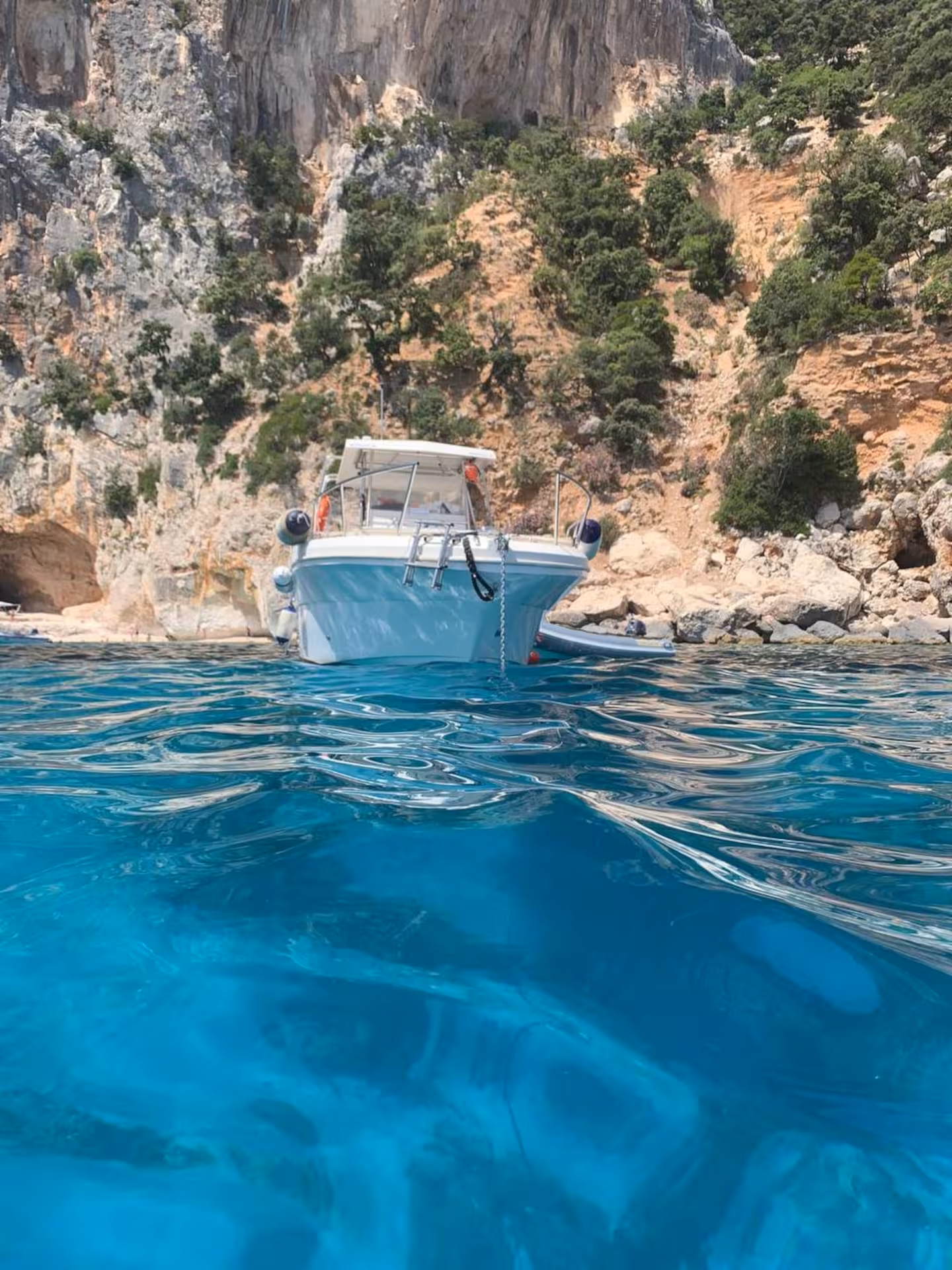 White boat anchored in the Gulf of Orosei, surrounded by turquoise waters and rugged cliffs near Cala Gonone.