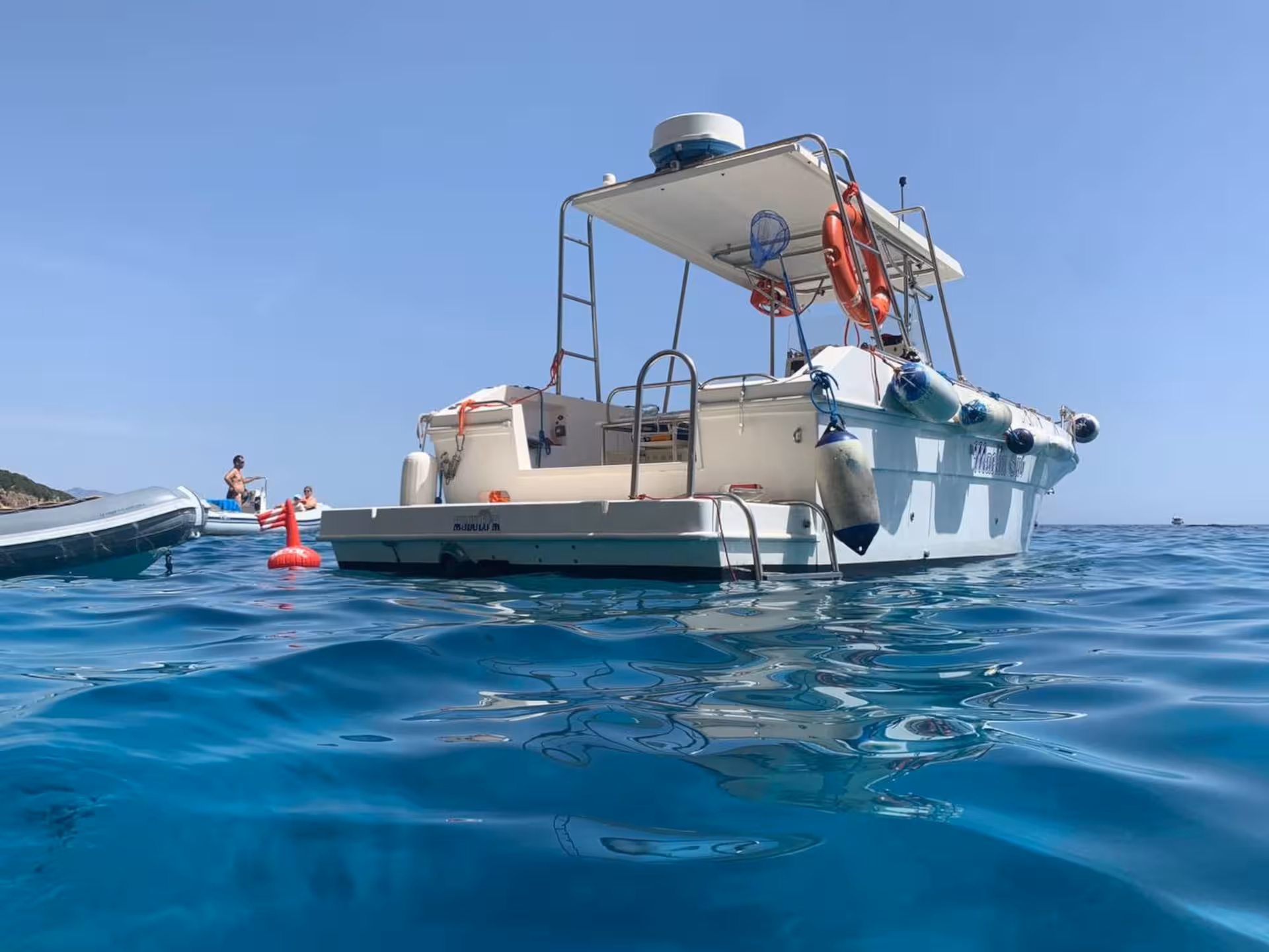 Tourists relaxing on a boat in the Gulf of Orosei, surrounded by calm, azure waters and a clear blue sky.