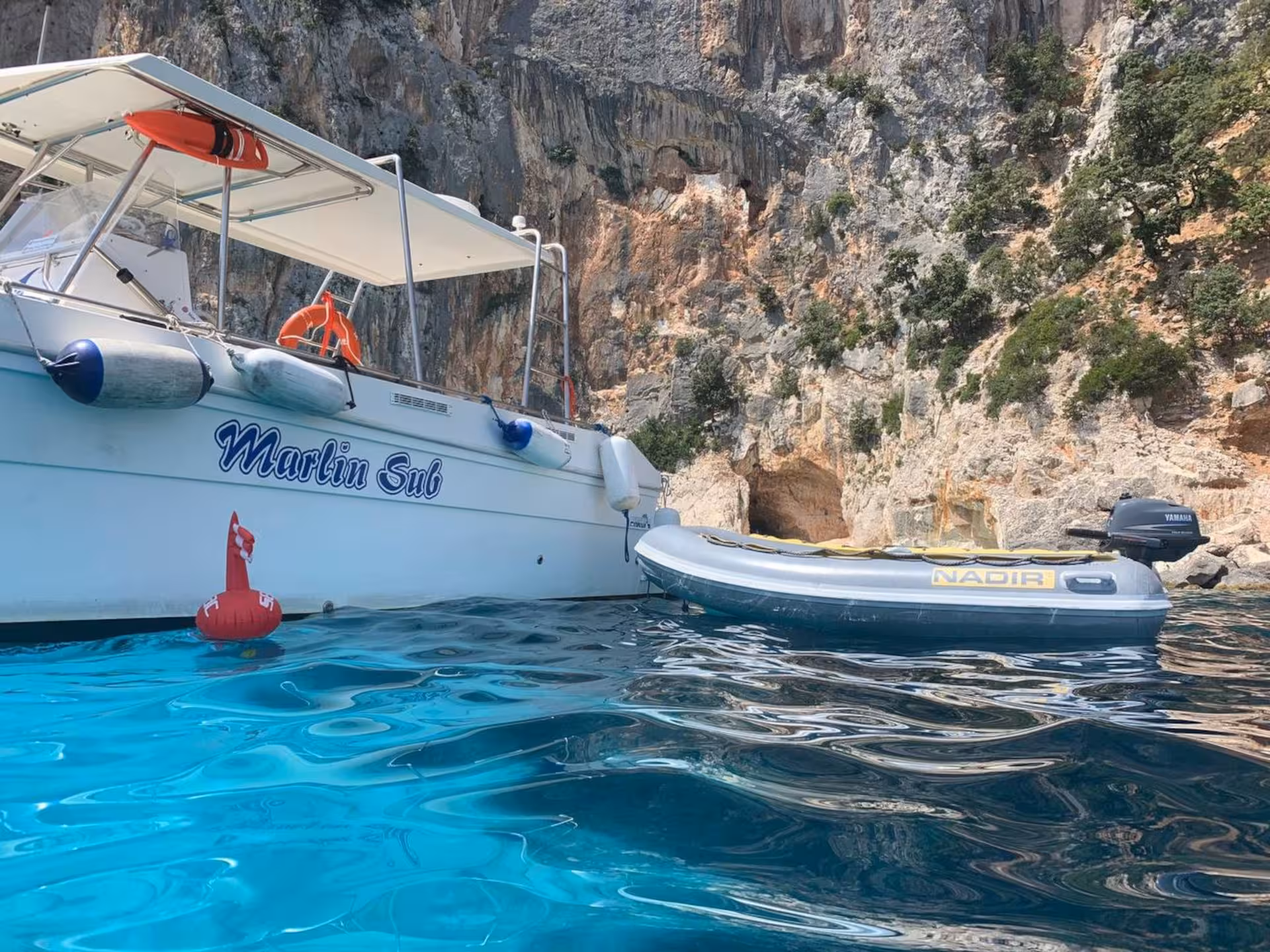 Tour boat and inflatable raft float in the Gulf of Orosei, showcasing rocky cliffs and clear blue waters near Cala Gonone.