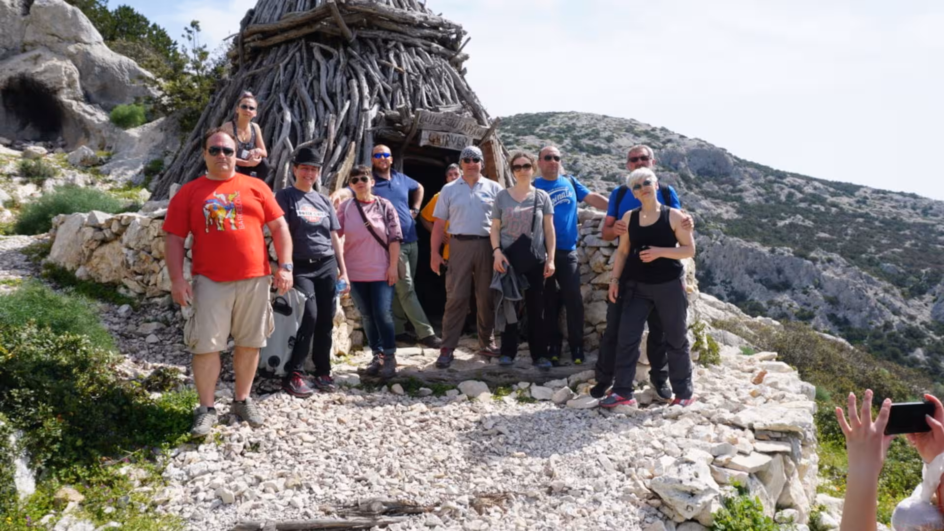 Group of travelers exploring a traditional shepherd's hut in Supramonte during the Jeep tour from Cala Gonone.