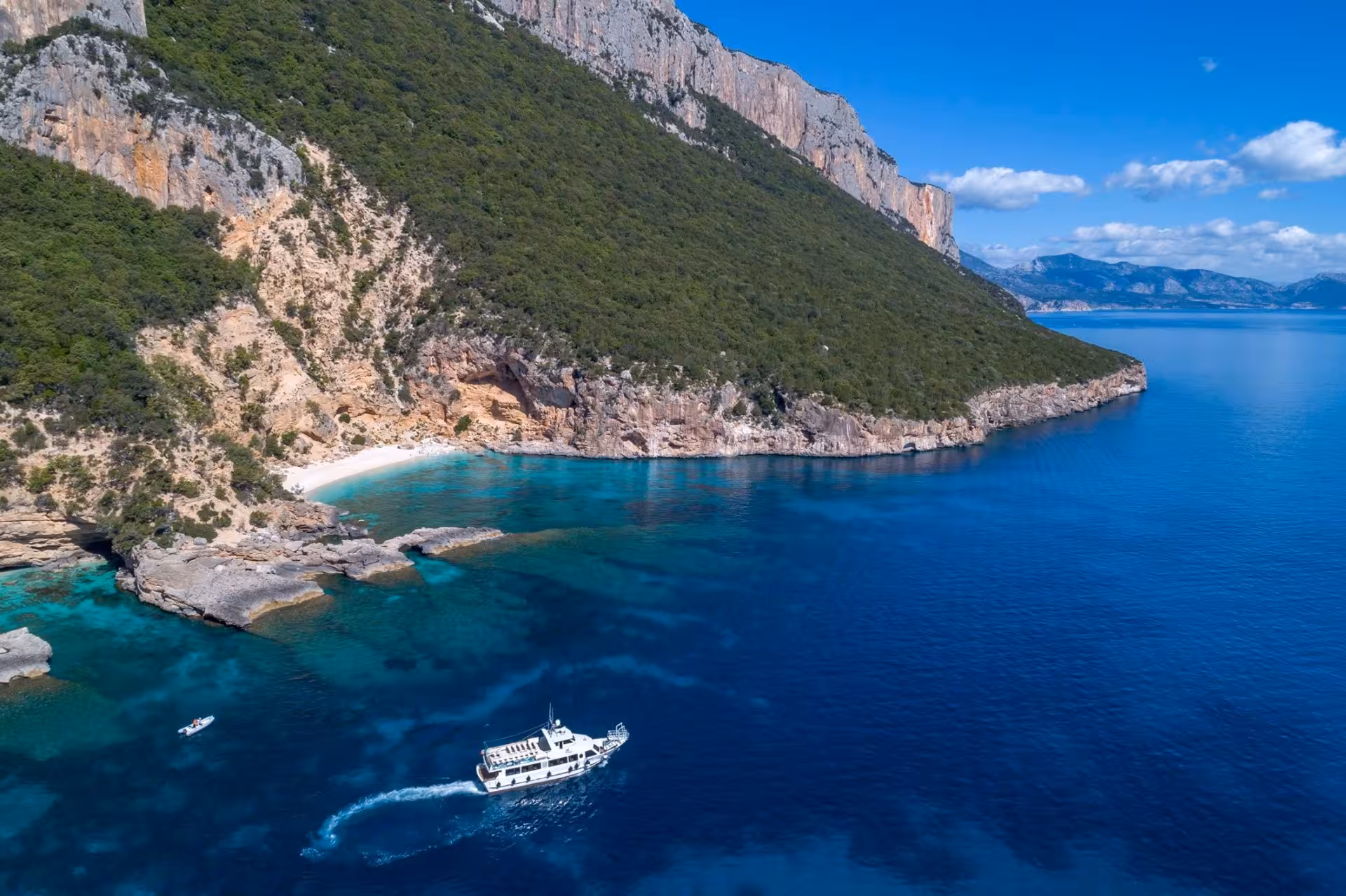 Scenic motorboat cruising along Cala Gonone's rugged coastline with crystal-clear blue waters and lush cliffs.