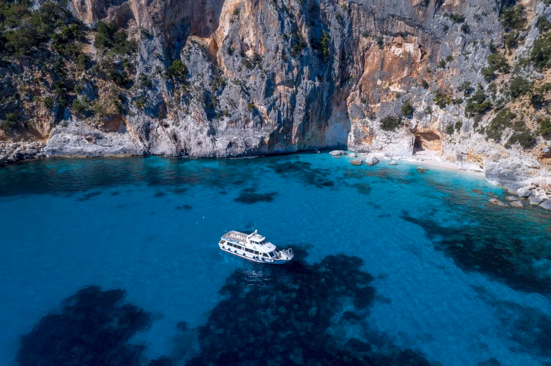 Aerial view of Cala Gonone beach with turquoise waters and cliffs, ideal for a motorboat tour to Bue Marino Caves.