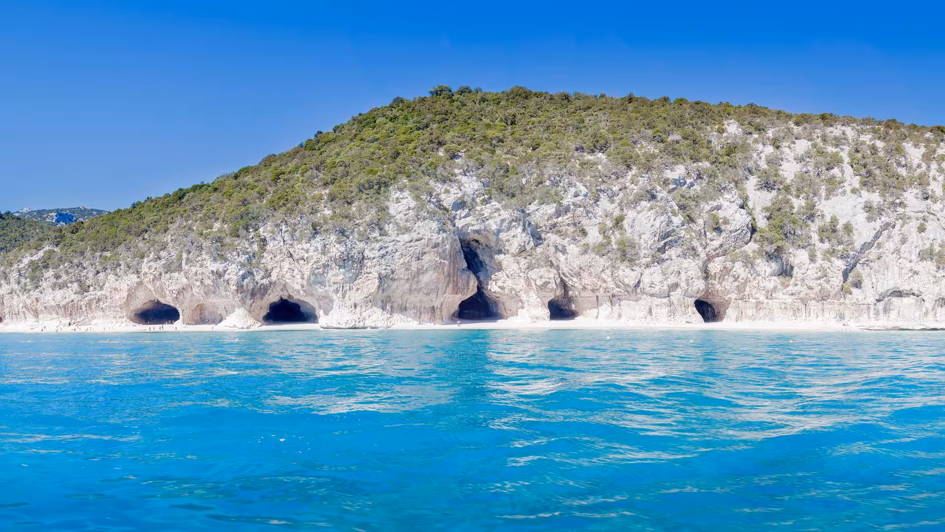 Scenic view of caves along the rocky coast of Cala Gonone, surrounded by azure waters and lush greenery.