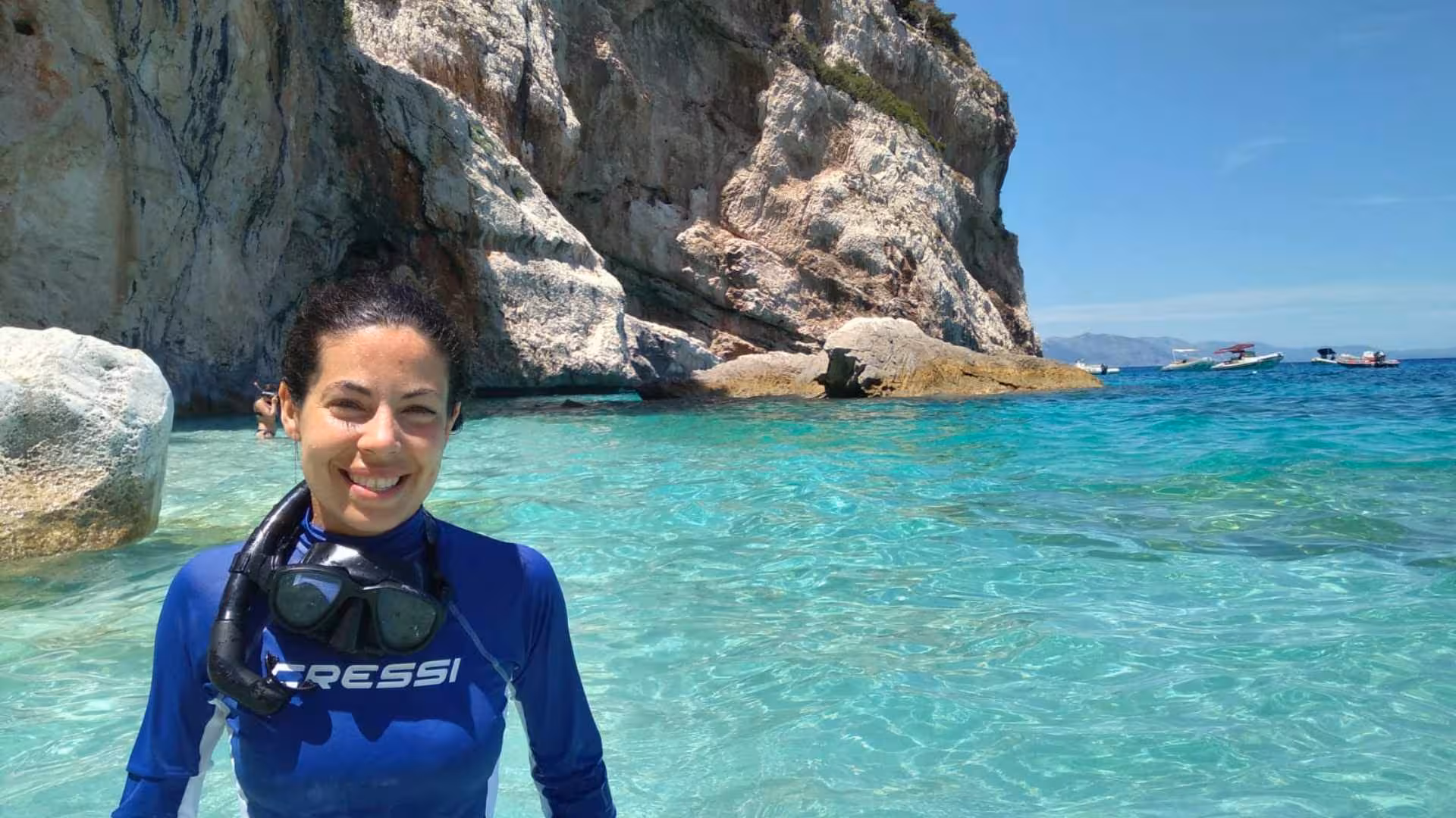 Smiling snorkeler in Cala Gonone with stunning rocky cliffs and turquoise waters in the Orosei Gulf background.