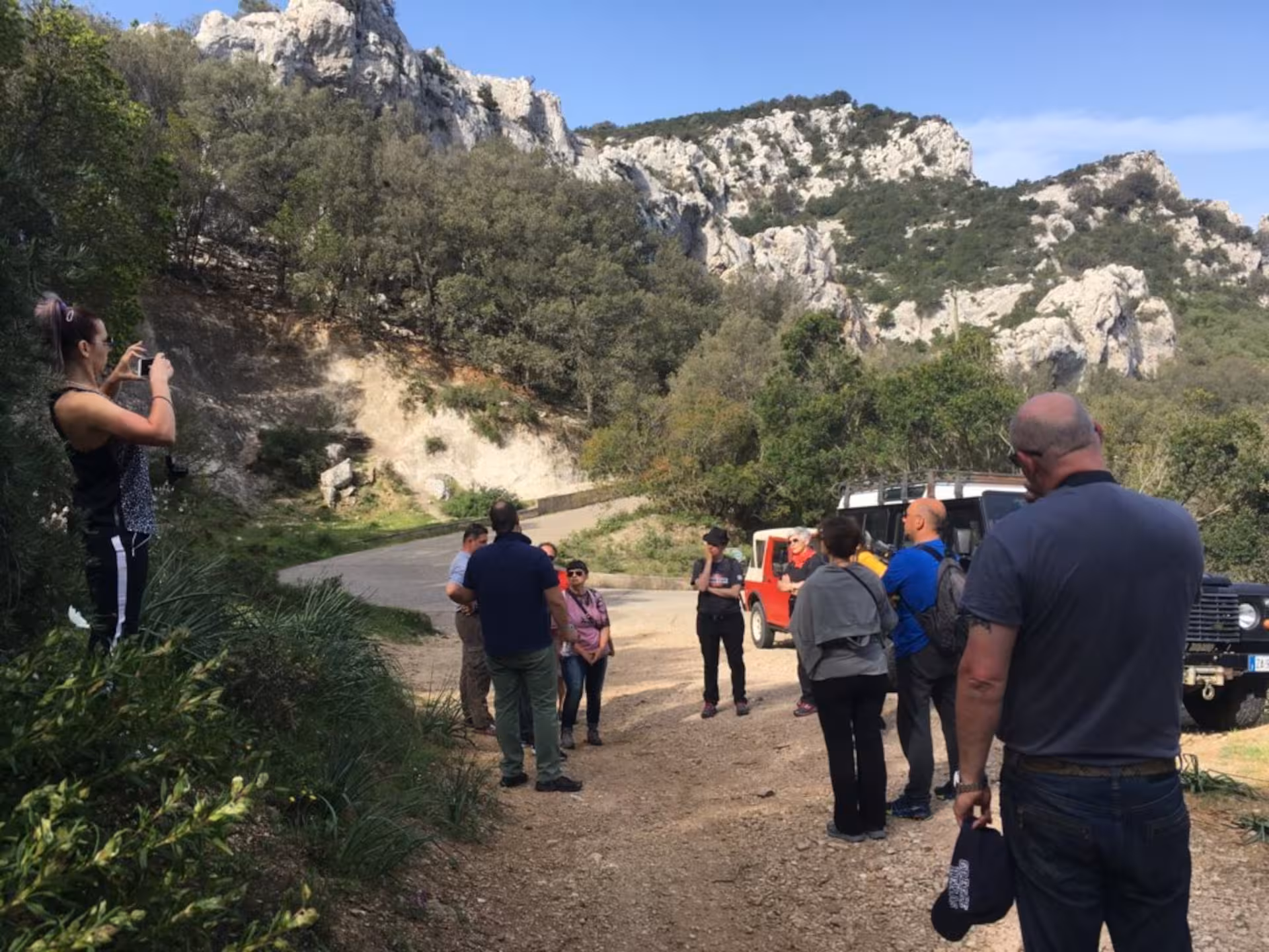 Tour group gathers near rugged cliffs on a Supramonte Jeep tour from Cala Gonone, enjoying the scenic views.