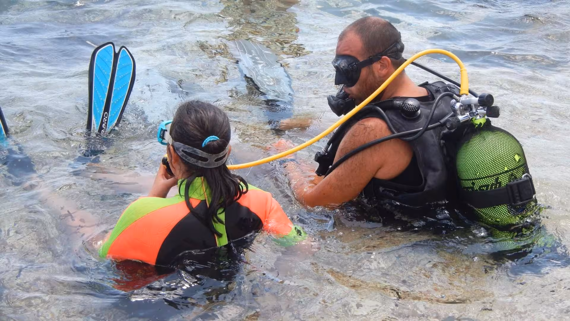 Diver instructs beginner during Cala Gonone underwater baptism, highlighting safe scuba introduction in clear waters.