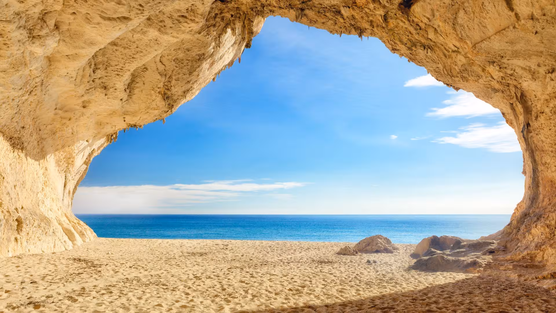View from a cave opening at Cala Luna beach showcasing sandy shores and vibrant turquoise waters under a clear sky.