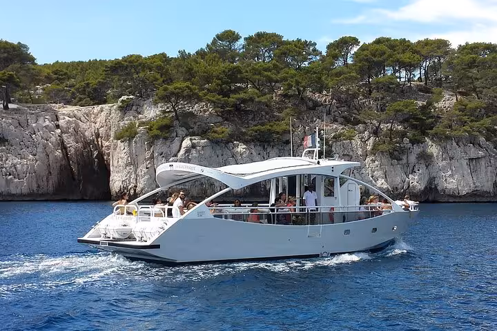 Tourists enjoying a scenic boat ride in the Calanques of Cassis, with lush greenery and limestone cliffs in the background.