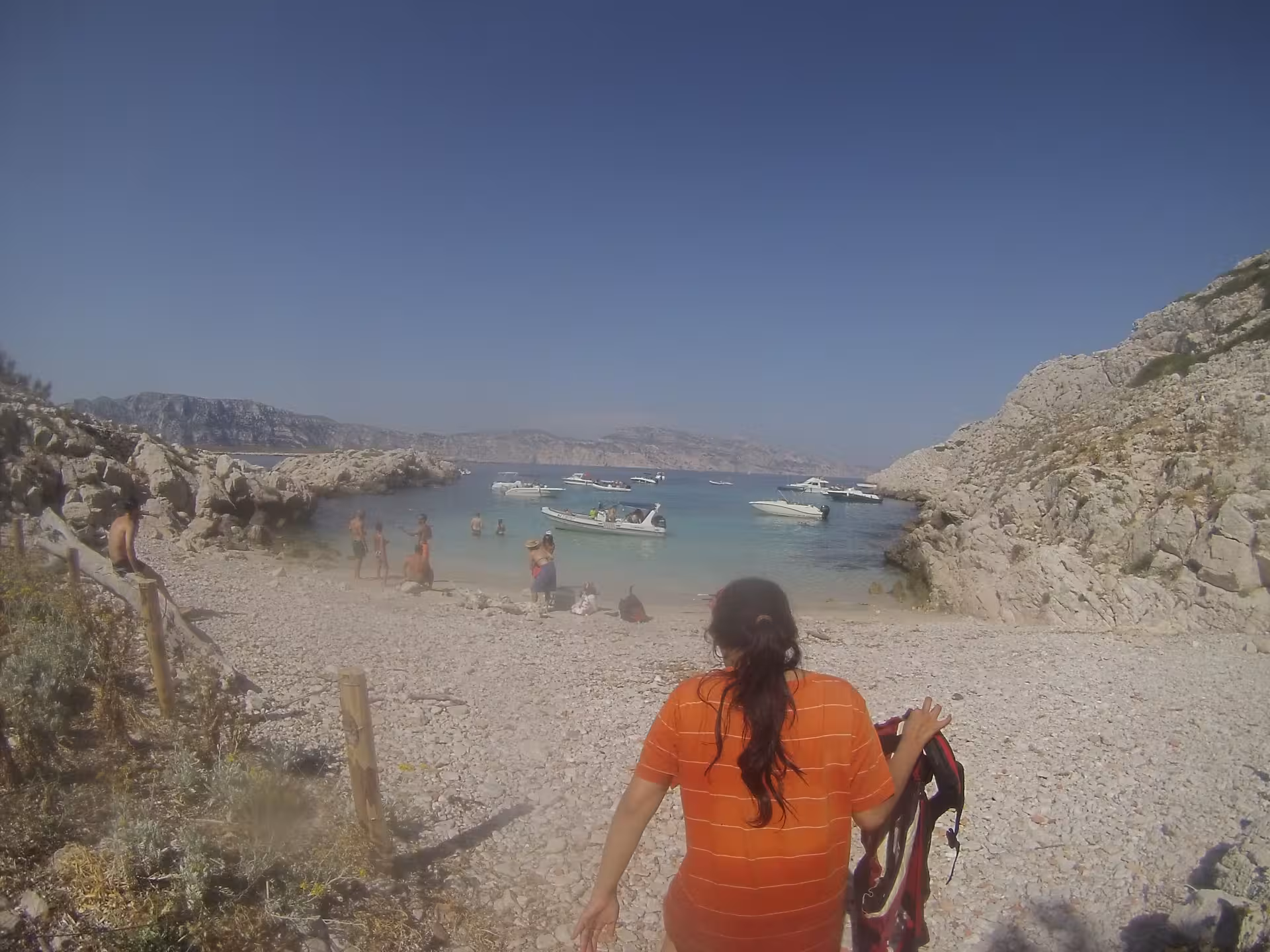 Hiker reaching a Calanques beach near Marseille before a kayak tour, rocky cove with boats on clear water