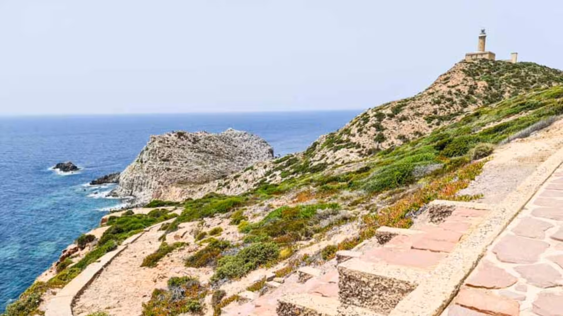 Scenic coastal view of Calasetta with rocky cliffs and a lighthouse, accessible through car hire for exploration.