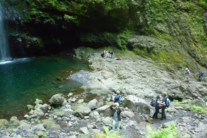 Visitors hike along rocky terrain near a tranquil waterfall pool on the Burned Green Cauldron adventure tour.