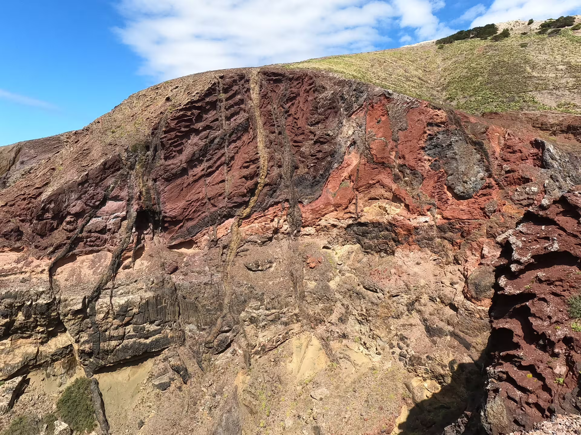 Dramatic coastal cliffs with vibrant red and brown hues on the Calheta Southwest Coastline Van Tour under a clear blue sky.