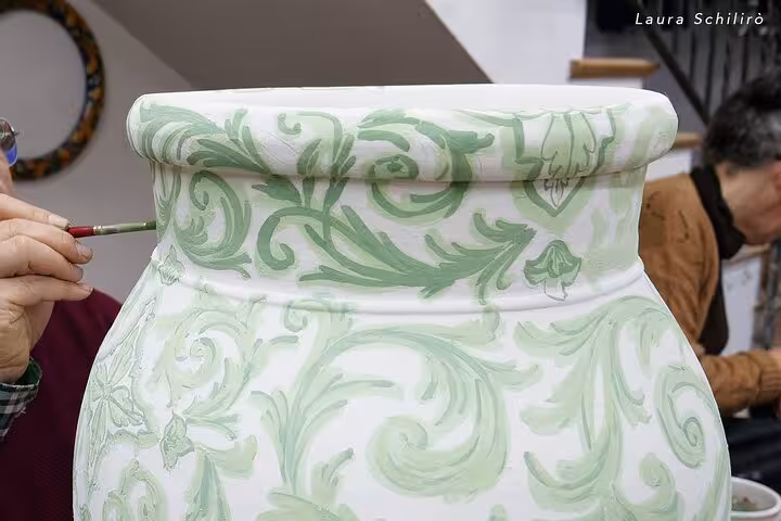 Close-up of vibrant green designs being painted on a large ceramic vase, highlighting Caltagirone's artistic heritage.