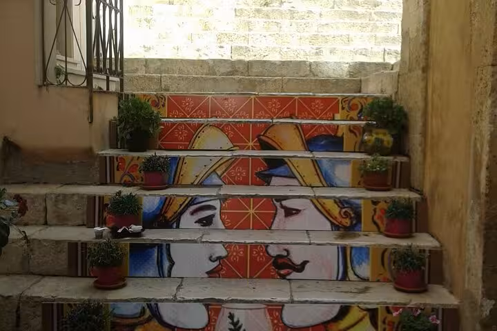 Vibrant painted steps in Caltagirone featuring artistic faces, surrounded by small potted plants, in Sicily.