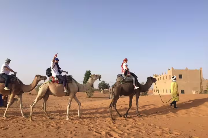 Camel caravan with travelers near desert kasbah, Morocco 12 days 11 nights desert tour from Agadir