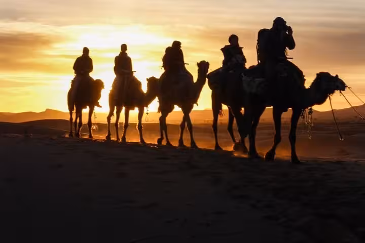 Camel caravan traversing Merzouga Desert at sunset during 3-day tour from Fes, offering a magical Sahara experience.