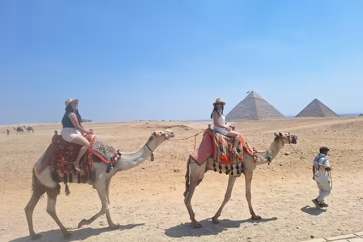 Travelers riding camels in the desert with the Pyramids of Giza in the background on a guided Cairo excursion.