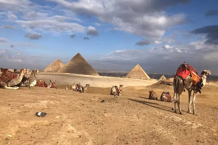 Camel resting near the Giza Pyramids under a dramatic sky, part of a private pyramids and Sphinx tour with lunch