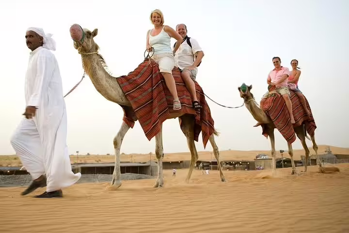 Tourists enjoying a camel ride led by a guide in a desert setting during a premium full-day safari experience.