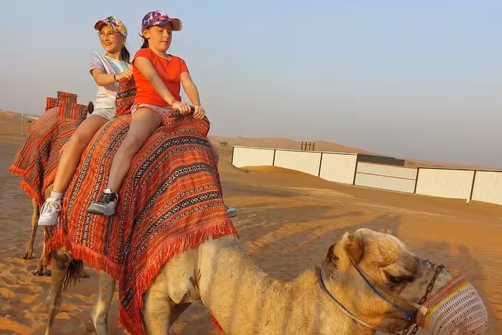 Camel ride in Ras Al Khaimah desert safari tour, kids on traditional saddle across golden dunes