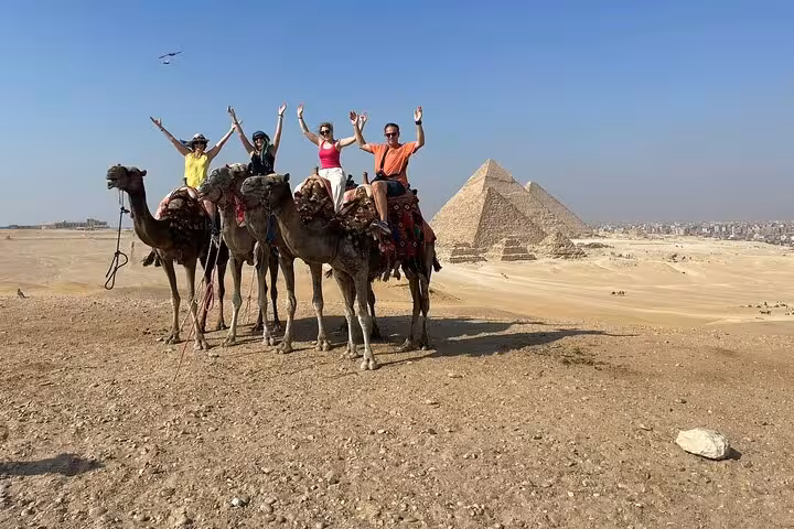 Camel ride at Giza Pyramids with travelers on Hurghada to Cairo day trip, desert panorama and pyramids view