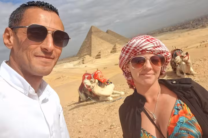 Tourists enjoying a camel ride with the iconic Pyramids of Giza in the background on a sunny Egypt tour.