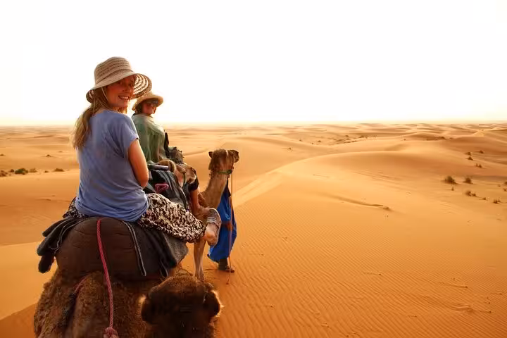 Smiling tourists enjoy a serene camel ride across the vast Sahara Desert landscape on a Fes to Marrakech tour.