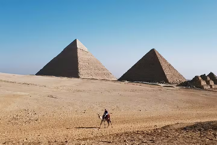 Camel rider crossing Giza Plateau with Great Pyramids in view on Cairo day trip tour from Old Cairo