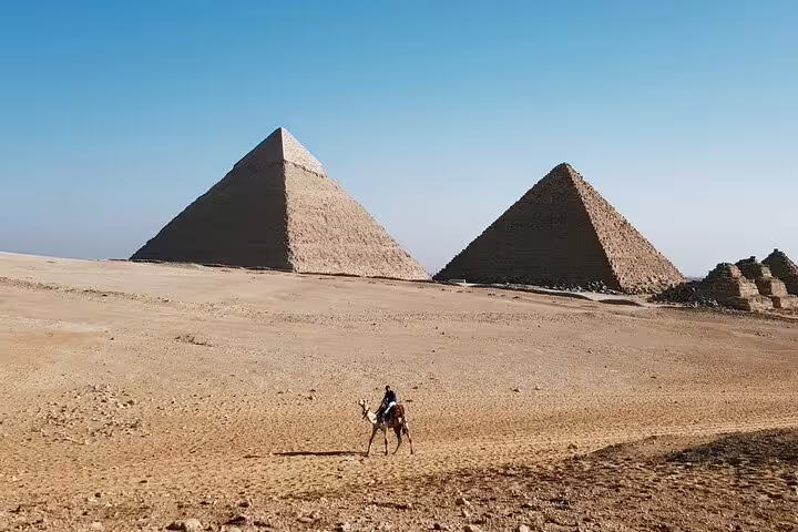 Camel rider crossing Giza Plateau with pyramids, scenic stop on private tour from NEMC and antiquities
