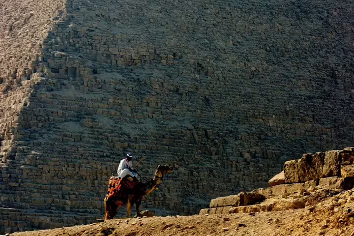 Camel rider at the base of the Great Pyramid of Giza, classic Cairo day tour experience with desert views
