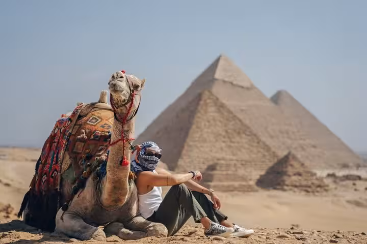 Camel and traveler resting with Giza Pyramids view on private Giza tour, plus Sphinx, Grand Egyptian Museum and bazaar