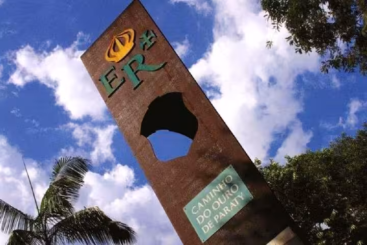 Entrance sign for Caminho do Ouro de Paraty against a vibrant blue sky, symbolizing the start of the cultural hike.