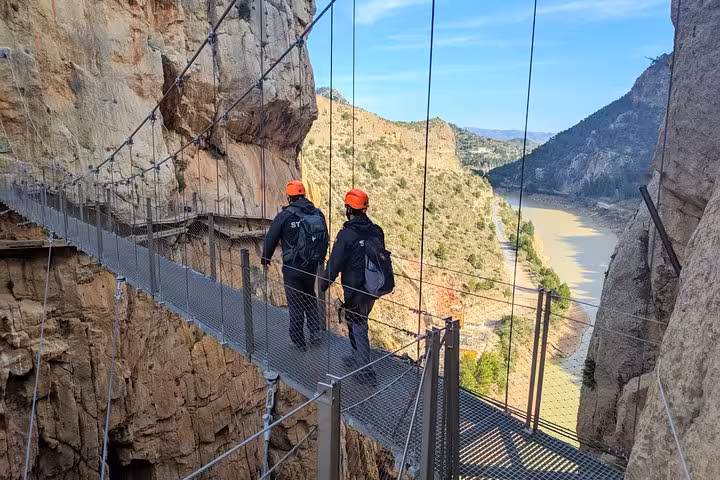 Two hikers with helmets cross a stunning suspension bridge on the Caminito del Rey small group tour from Malaga.